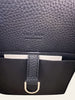 The Row Soft Margaux 10 Black Grained Calfskin — interior view: close-up of the interior flap showing The Row's embossed logo on the black leather, with a stitched tab and D-ring closure strap.
